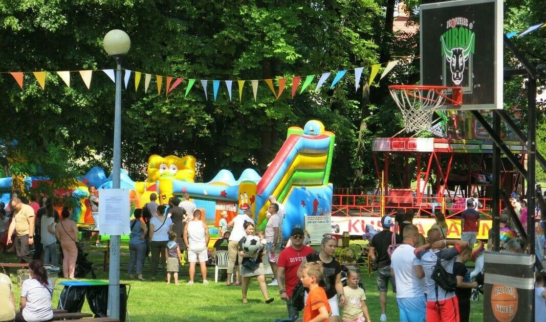 Dzieci w parku, w tle dmuchańce i kosz do gry w koszyk&oacute;wkę